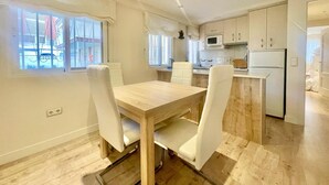 Een moderne keuken met witte kasten, een magnetron en een koelkast. Er is een eethoek met een houten tafel en witte stoelen.