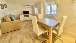 Een woonkamer met een bank, een televisie, een eettafel en stoelen.