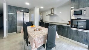 Eine moderne Küche mit Essbereich, ausgestattet mit einem Edelstahl-Kühlschrank, einer Mikrowelle und einem Backofen, mit einem Tisch für zwei Personen und einer Obstschale.