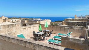 A rooftop terrace with a table and chairs, a green umbrella, and lounge chairs.
