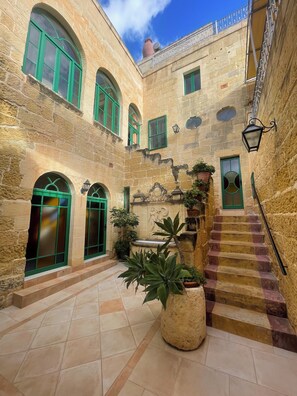 A courtyard with stone walls, green-framed windows, a fountain, and a staircase. - Historic Farmhouse with Courtyard, Kitchen Terrace and Rooftop Pool (In-Nadur)