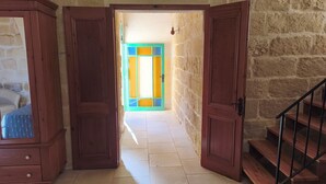 An open wooden door leading to a room with a bed and a view of a colorful door.