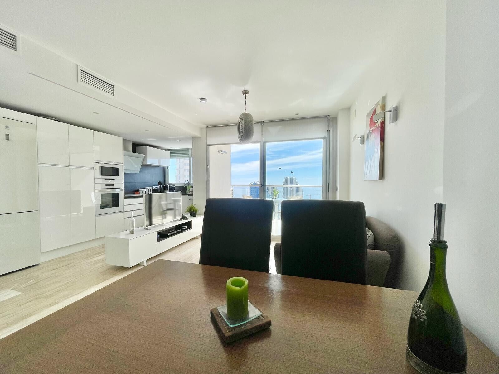 A modern apartment with a kitchen, dining area, and a balcony with a city view.