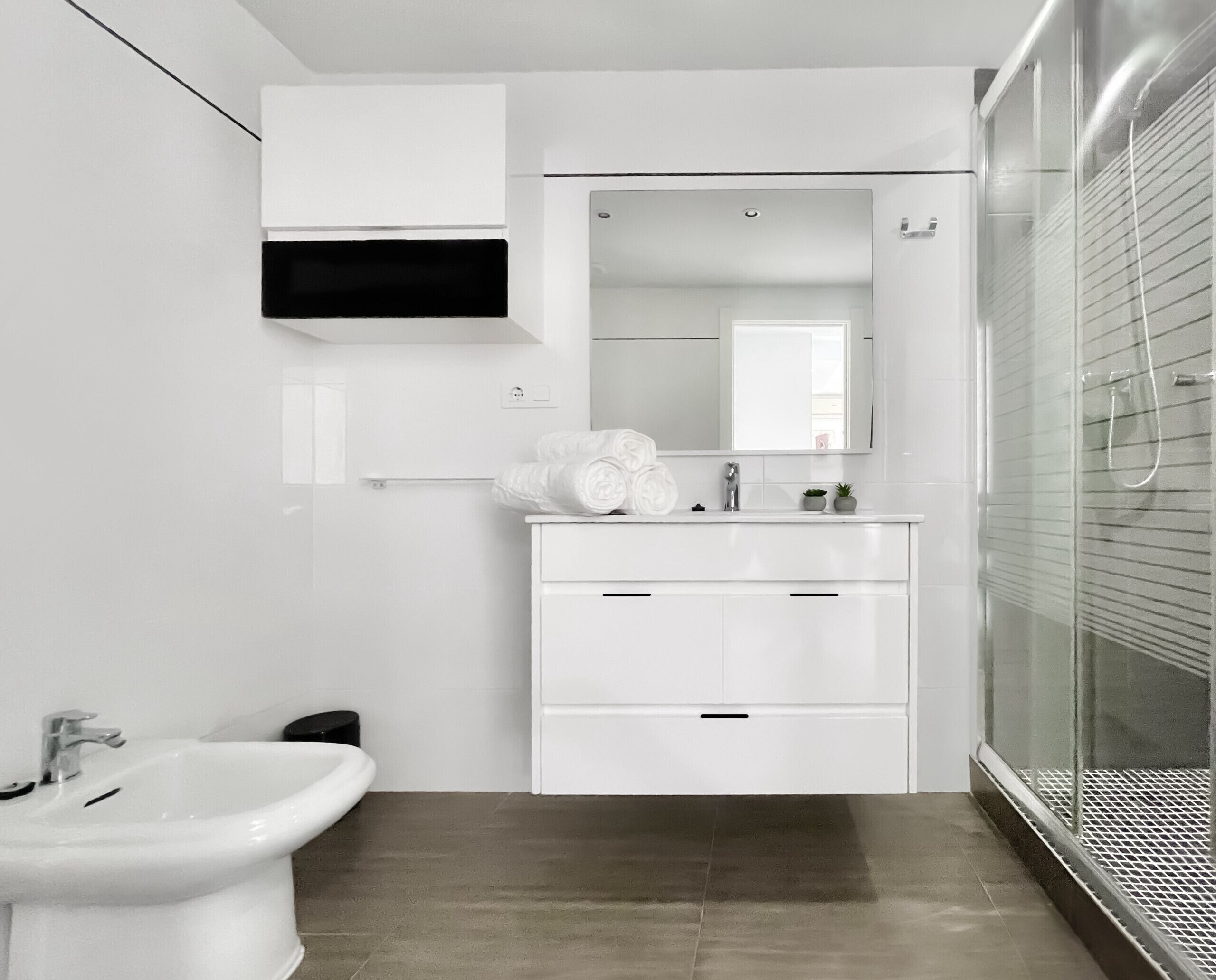 A modern bathroom with a white vanity, a mirror, a shower enclosure, and a bidet.