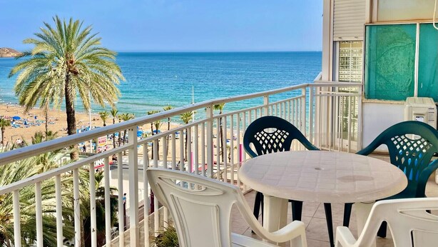 Un balcón con vista a la playa y el océano, con una mesa redonda y sillas.