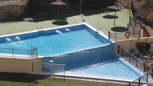 A rectangular swimming pool with a metal railing, surrounded by a grassy area with umbrellas and a staircase leading to a deck. - MIRADOR DEL MEDITERRANEO N172 (Benidorm)