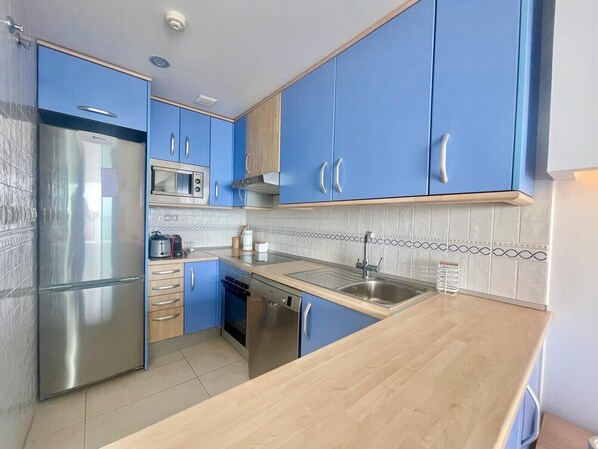 A modern kitchen with blue cabinets, stainless steel appliances, and a wooden countertop. - MIRADOR DEL MEDITERRANEO N172 (Benidorm)