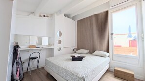 A bedroom with a bed, a desk with a mirror, a chair, and a window with a view of the outside. - Naturiste Cap d'Agde Port Soleil 146 (Agde)