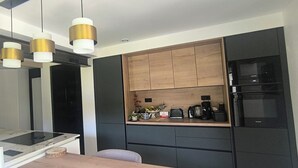 A modern kitchen with a black refrigerator, a built-in oven, and a wooden countertop. There are three pendant lights with gold accents.