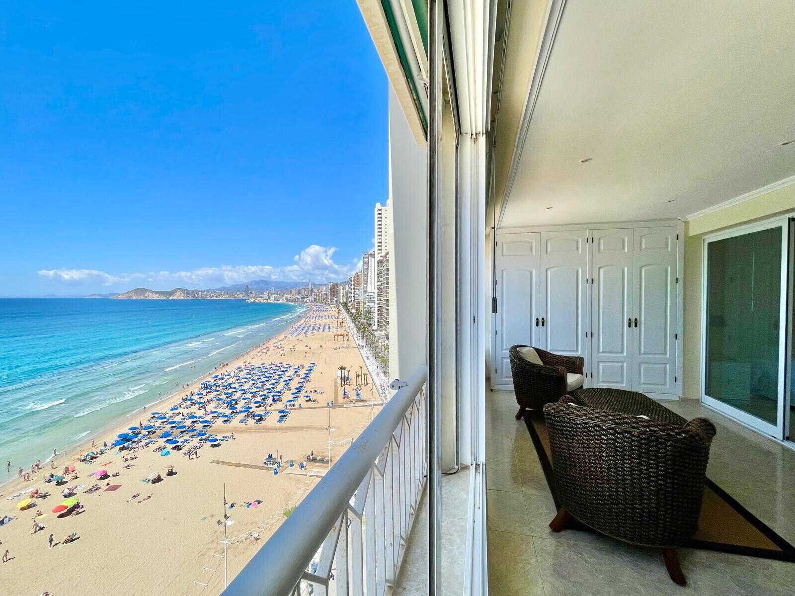 Un balcon donnant sur une plage, une chaise en osier et une porte blanche.