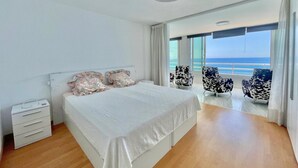 Un dormitorio moderno con una cama grande, una mesita de noche y vistas al océano a través de amplios ventanales.