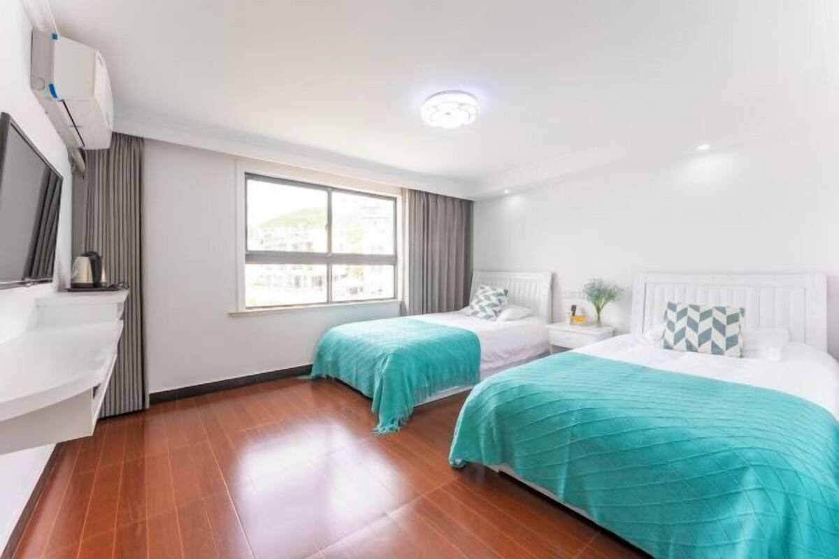 Une chambre d’hôtel avec deux lits, une fenêtre, un lavabo blanc et un luminaire au plafond.