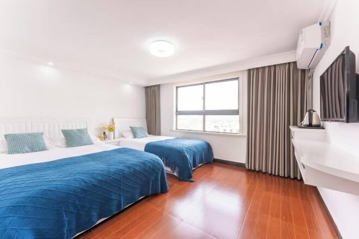 Une chambre d’hôtel avec deux lits, une grande fenêtre, un radiateur blanc et un canapé blanc.