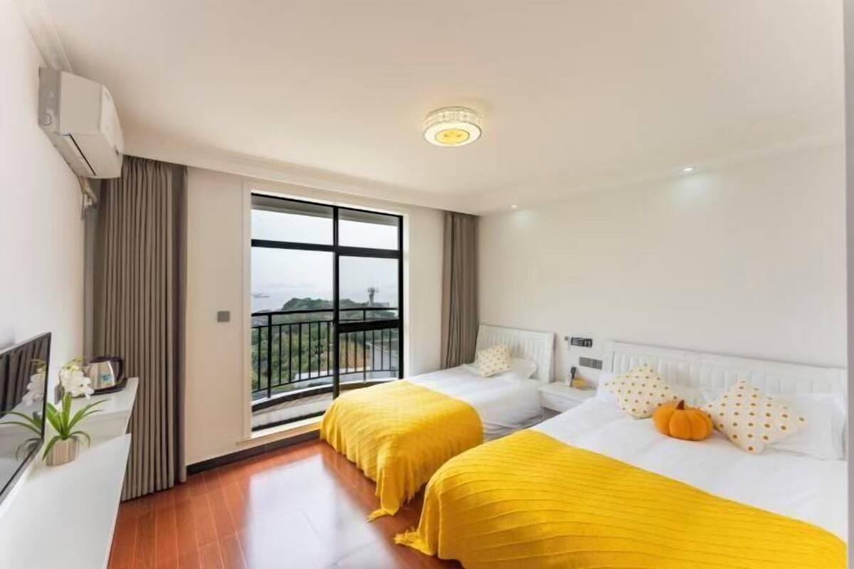 Une chambre d’hôtel avec deux lits, un balcon, une grande fenêtre et un luminaire au plafond.