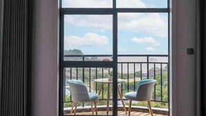 Un balcón con dos sillas y una mesa, con vista a una ciudad y un cuerpo de agua, incluyendo un puente.