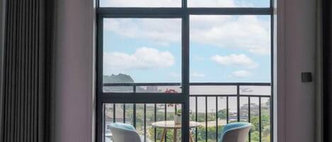 A balcony with two chairs and a table, overlooking a cityscape with a body of water and a bridge.
