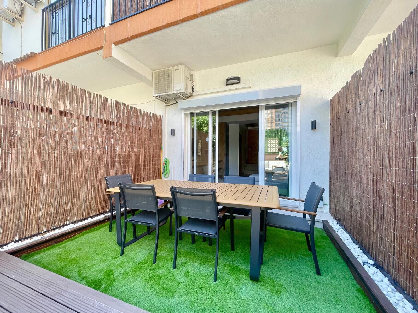 Eine Terrasse mit Tisch und Stühlen, ein Holzzaun und ein Bereich mit künstlichem Rasen.
