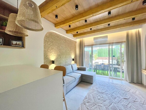 A modern living room with a stone accent wall, a sofa, a dining table, and a large window with a view of the outdoors.