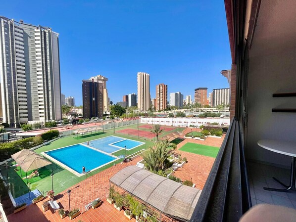 Un edificio de gran altura con piscina en la azotea y canchas de tenis, rodeado de otros edificios altos.