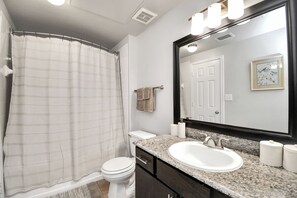 A bathroom with a white toilet, a shower curtain, a sink with a mirror, and a towel rack.