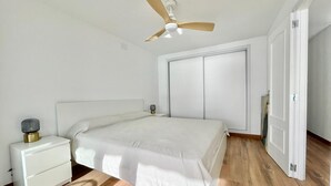 A bedroom with a bed, a nightstand, a ceiling fan, a wardrobe, and a door.