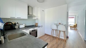 A modern kitchen with white cabinets, a grey countertop, and a dining area with two white chairs.