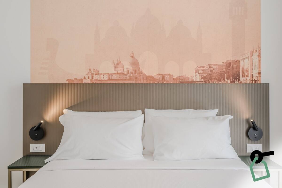A hotel room with a bed, two bedside tables, and a wall-mounted lamp.