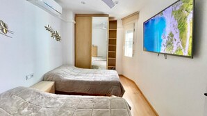 A bedroom with two beds, a ceiling fan, a large TV, and a wardrobe. - EMALCO SEAFRONT MODERN APARTMENT A061 (Benidorm)
