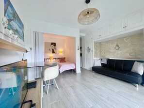 A modern apartment with a glass dining table, a black sofa, a bed with a pink and white patterned bedspread, and a wall with heart-shaped designs.