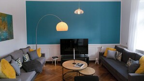 Ein modernes Wohnzimmer mit zwei grauen Sofas, einem runden Couchtisch, einem Fernseher und einer großen Wand in Türkis.