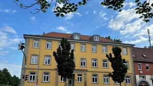 Ein gelbes Gebäude mit vielen Fenstern und einem roten Dach, an einer Straßenecke mit parkenden Autos.
