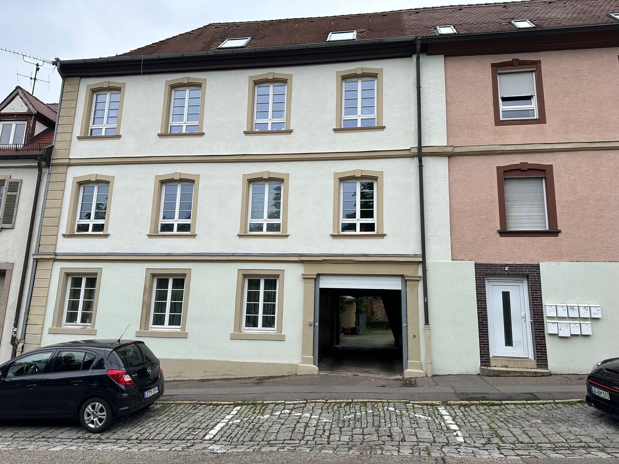 Ein mehrgeschossiges Gebäude mit Hauseingang im Erdgeschoss, einer Garagentür und einer Reihe von Fenstern in den oberen Stockwerken.