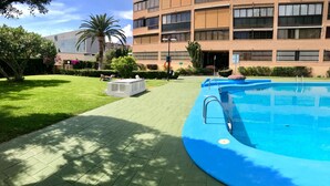 A swimming pool area with a paved walkway, a palm tree, and a building in the background. - ALBAIDA PARK BENIDORM LEVANTE (A137) (Benidorm)