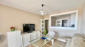 A living room with a sofa, a glass table, a TV on a cabinet, a fan, and a mirror on the wall. - ALBAIDA PARK BENIDORM LEVANTE (A137) (Benidorm)