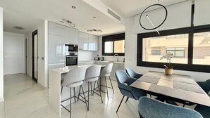 Une cuisine moderne avec des armoires blanches, un four encastré et un coin repas comprenant une table et des chaises.