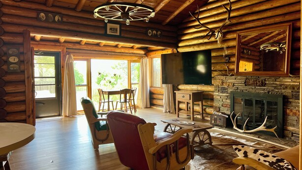 Ein Blockhauskamin mit Kamin, Holzmöbeln und einem großen Fernseher.