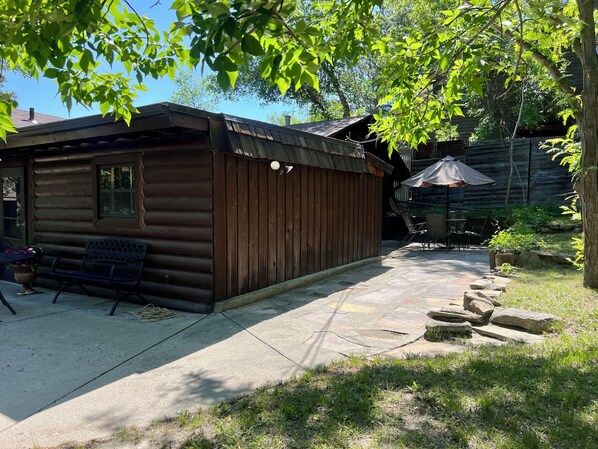 A wooden cabin with a patio area, a bench, and a table with chairs.