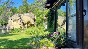 Ein Haus mit einer großen Felsformation im Garten, einem Holzzaun und verschiedenen Pflanzen und Blumen.