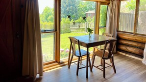 Eine Holzhütte mit Esstisch und Stühlen, großen Fenstern und Blick auf einen umzäunten Garten.