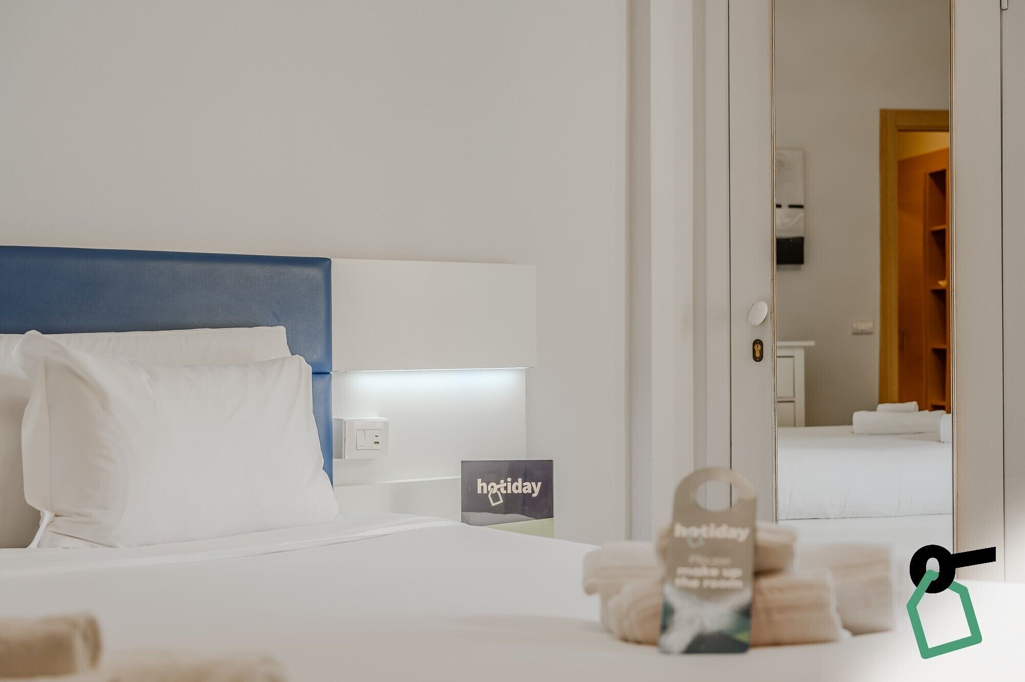 A hotel room with a bed, a nightstand, a mirror, and a door leading to a bathroom.
