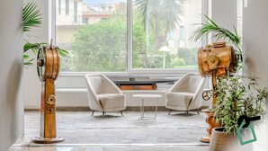 Ein Zimmer mit großem Fenster, zwei Sesseln, einem kleinen runden Tisch und zwei Ventilatoren im Vintage-Stil.