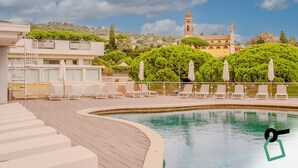 Ein Poolbereich mit Liegestühlen und Blick auf historische Gebäude im Hintergrund.