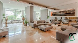 Eine geräumige Lobby mit einer großen Sitzgruppe, einem Kunstwerk im modernen Stil und großen Fenstern mit Blick ins Freie.