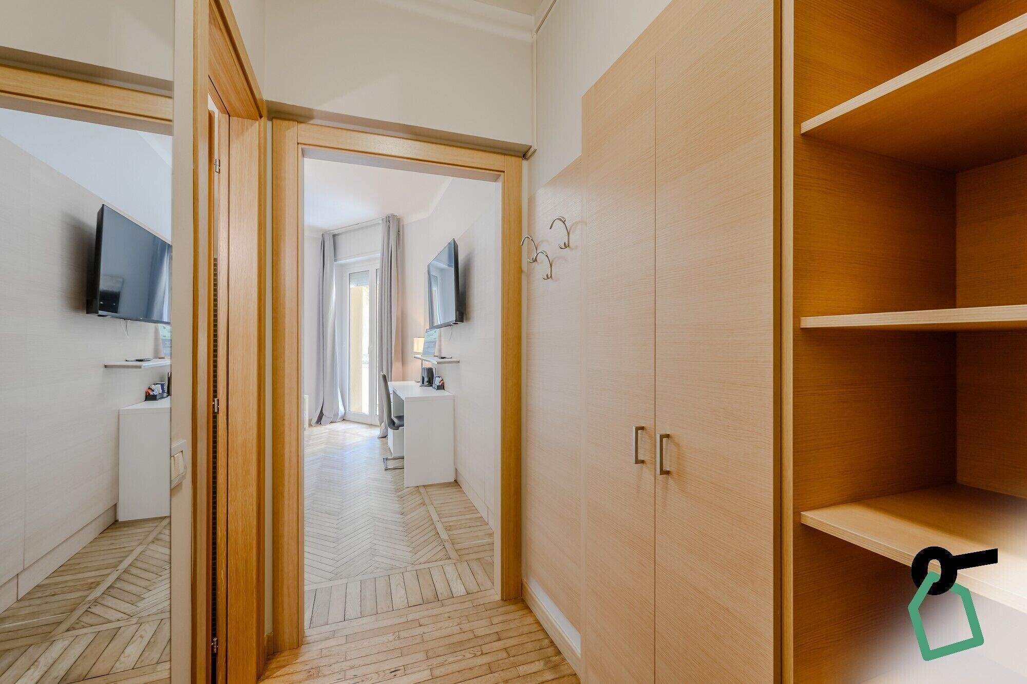 Habitación de hotel con un armario de madera, un televisor montado en la pared y un escritorio con una silla.