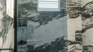 A bathroom with a glass shower enclosure and marble walls.