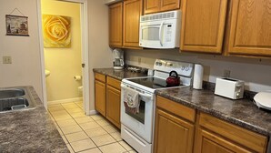 A kitchen with wooden cabinets, a microwave, a stove, a kettle, and a toaster. - #05 Charming 2-bedroom apartment in Lorain with AC, WiFi (Lorain)