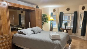 A hotel room with a large bed, wooden wardrobe, a mirror, a bedside table with a lamp, and a view of the street through the window. - #05 Charming 2-bedroom apartment in Lorain with AC, WiFi (Lorain)