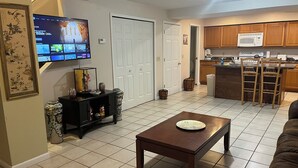 A living room with a TV, a coffee maker, and a kitchen area with wooden cabinets and a microwave. - #05 Charming 2-bedroom apartment in Lorain with AC, WiFi (Lorain)