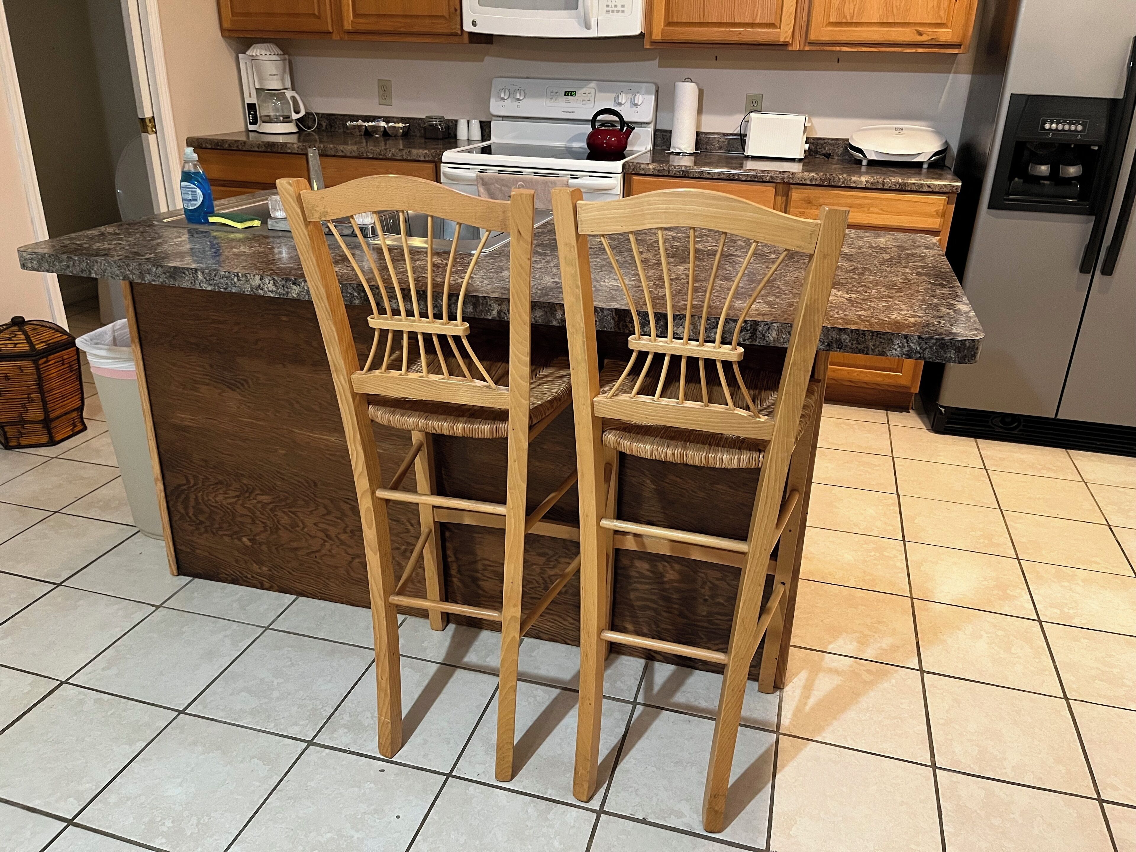 Een keuken met houten stoelen, een granieten aanrecht, een fornuis, een magnetron en een koelkast.