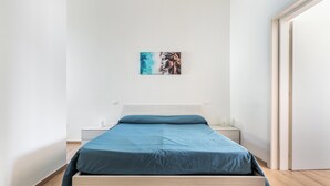 Ein schlichter Schlafzimmerbereich mit Bett, Nachttisch und Wandbild.